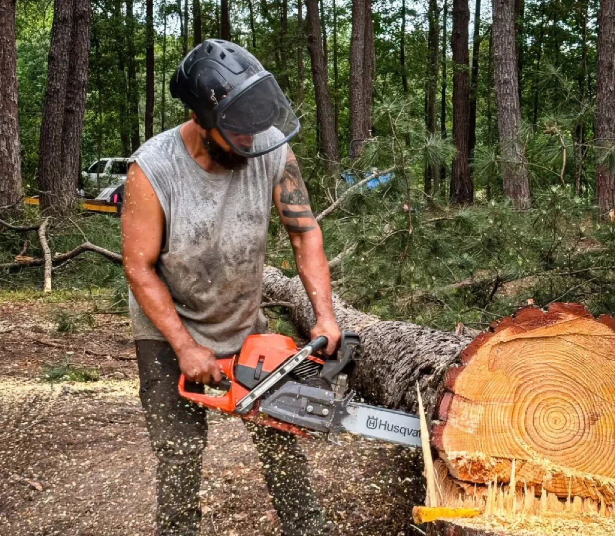 LoyalTree owner Michael Williams cutting through a large log with a chainsaw